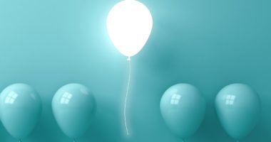 lit-up balloon on aqua background above four aqua balloons